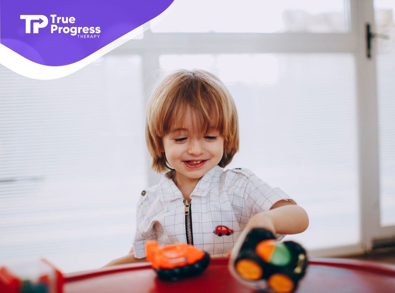 Young child smiling while playing with toy cars during an ABA therapy activity.